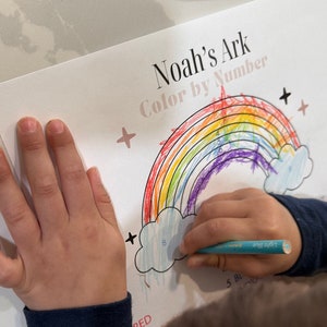 May include: A child colors a rainbow with crayons. The rainbow is labeled "Noah's Ark Color by Number".