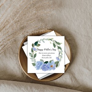 Puede incluir: Una tarjeta blanca con una corona floral azul y el texto "Feliz D&iacute;a de la Madre. Ella es m&aacute;s preciosa que los rub&iacute;es. Proverbios 31:10."