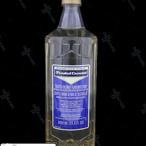 May include: A clear plastic bottle of Starbucks Toasted Coconut flavored syrup with a tan cap. The blue label displays the product name, ingredients, and a volume of 1000 ML (33.8 FL OZ). A separate white tag indicates the date June 2026.