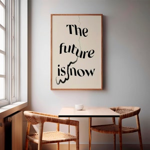 May include: A framed print with the words "The future is now" in black lettering. The print is in a light wood frame and hangs above a small table and two wooden chairs. A white teacup sits on the table.