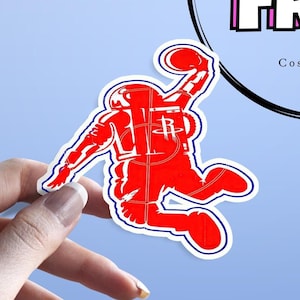 Puede incluir: Pegatina de astronauta roja y azul con una pelota de baloncesto en la mano, haciendo un mate. El astronauta lleva un traje espacial con un logotipo de los Houston Rockets rojo y azul en el pecho.