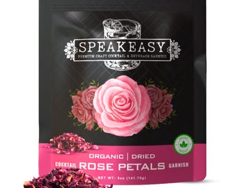 Może przedstawiać: Czarny i różowy pakiet suszonych płatków róż do koktajli. Na opakowaniu widnieje napis "SPEAKEASY" i "COCKTAIL ROSE PETALS GARNISH". Waga netto wynosi 141,75 g. Przed nim leży stos suszonych płatków róż.