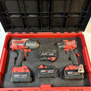 Peut inclure: Une mallette à outils rouge contenant deux visseuses à chocs Milwaukee et trois batteries M18 RedLithium XC 5.0. La mallette est ouverte, révélant les outils à l'intérieur.