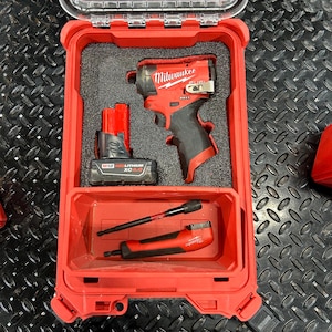 May include: A red Milwaukee tool case with a black and red impact driver, a red battery, and a red and black screwdriver bit holder.