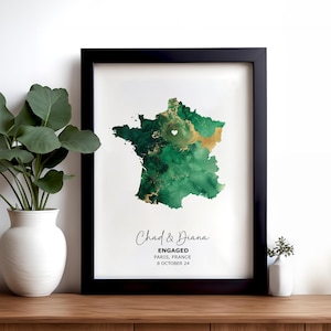 May include: A green and gold watercolour map of France with a white heart in the centre. The text below reads "Chad & Diana Engaged Paris, France 8 October 24".