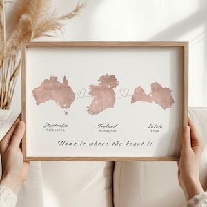 Peut inclure: Impression encadrée avec des cartes de l'Australie, de l'Irlande et de la Lettonie, reliées par des cœurs. Le texte comprend "Australie Melbourne", "Irlande Monaghan", "Lettonie Riga" et "Home is where the heart is". Le cadre est marron clair.