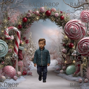 May include: A young child walks toward the viewer in a winter wonderland scene. The backdrop features a Christmas archway with ornaments and giant lollipops. The scene is decorated with candy canes, lollipops, and a snowy ground, creating a festive holiday atmosphere.
