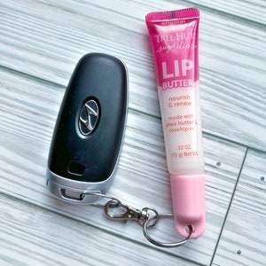 May include: A pink lip balm tube with a silver key chain attached. The lip balm is labeled "Tree Hut sugarlips Lip Butter" and says "nourish & renew made with shea butter & rosehip oil .52 oz. (15 g) Net Wt."