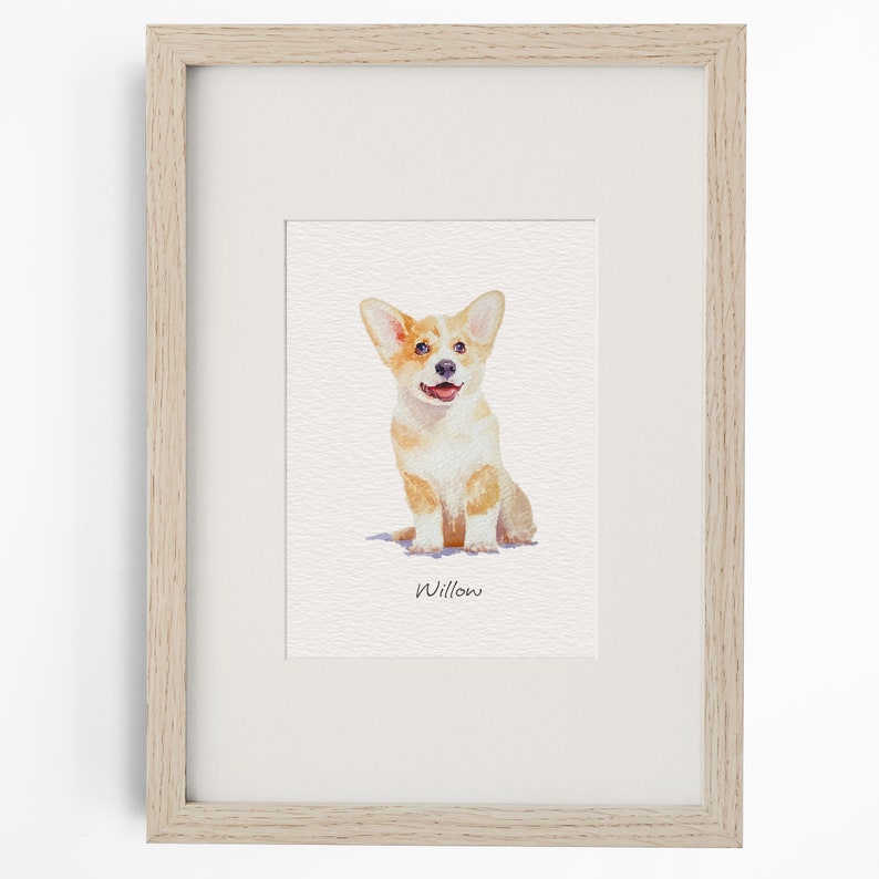 May include: A framed watercolour print featuring a tan and white Corgi puppy sitting down. The dog has large ears, a black nose, and an open mouth. Below the illustration, the name Willow is written in black cursive script on a white background.