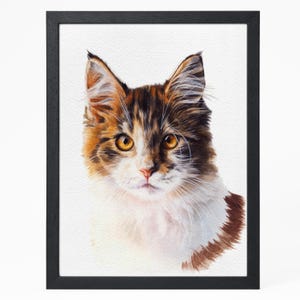 May include: A framed watercolour painting of a cat's face. The cat has brown, orange, and white fur, with yellow eyes and a pink nose. The artwork is set against a white background and framed in black.