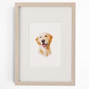 May include: A framed watercolour painting of a golden retriever dog head. The dog has golden fur, a black nose, and an open mouth showing a pink tongue. The artwork is set within a light-coloured wooden frame with a white mat border surrounding the image.