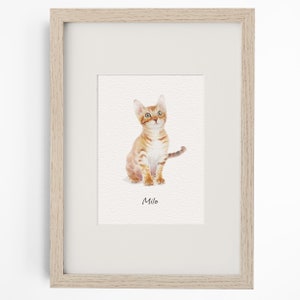 May include: A framed watercolour print featuring an orange tabby kitten sitting and looking upward. The kitten has light orange fur with darker stripes and green eyes. Below the kitten, the name Milo is printed in a simple black sans-serif font.