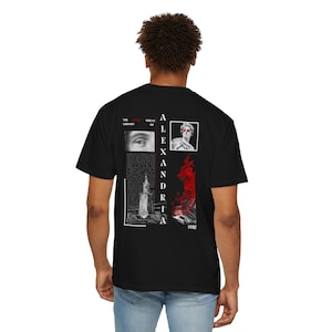 May include: Black t-shirt featuring a graphic print of a building, a person with a blindfold, and an eye. The text "THE GREAT LIBRARY OF ALEXANDRIA" is printed in red on the shirt.