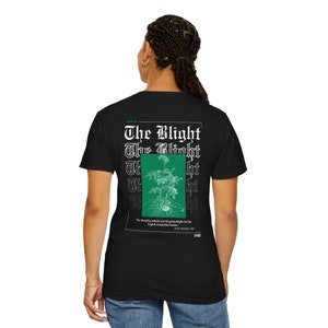 Puede incluir: Camiseta negra con un gráfico verde de una planta y el texto "The Blight" repetido en una fuente gótica. El texto "The Blight" se repite cinco veces, con cada repetición ligeramente desplazada de la anterior. El texto "The Blight" está en blanco. El texto "The simplicity, indeed, and the potato-blight, but the English created the famine." está impreso en una fuente más pequeña debajo del gráfico. El texto "1845-49" está impreso en una fuente más pequeña encima del gráfico. El texto "P.S.R" está impreso en una fuente más pequeña debajo del texto.