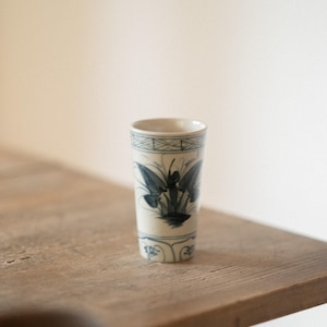 Puede incluir: Un jarrón de cerámica blanca con un diseño floral azul. El jarrón está sobre una mesa de madera.