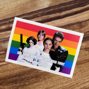 May include: A sticker with a rainbow background and a group of four people. The text on the sticker reads "We love our gay son and thot daughter".