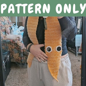 Puede incluir: Una bufanda de crochet de color amarillo y naranja con dos círculos blancos en la parte delantera. La bufanda se lleva alrededor del cuello de una persona.