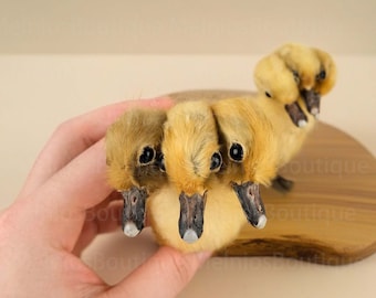 May include: Three yellow ducklings with black eyes and beaks are clustered together, looking up at the camera. They are on a wooden surface.