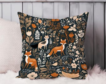 May include: Square decorative pillow with a dark teal background featuring a repeating pattern of foxes, flowers, and foliage in shades of orange, tan, and white. The pillow is placed on a white fluffy surface.