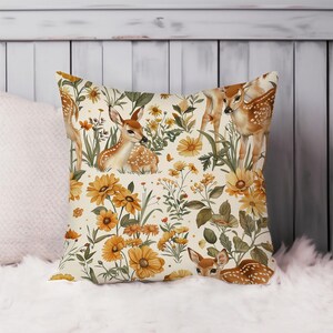 May include: Square decorative pillow featuring a watercolor design of deer and yellow flowers. The pillow has a cream-colored background with a repeating pattern of deer, daisies, and other wildflowers. The deer are brown with white spots.