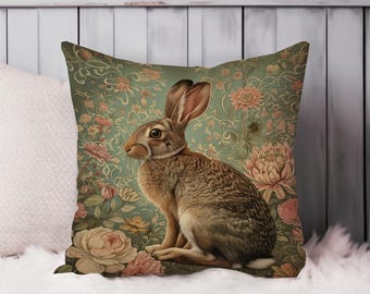 May include: Square decorative pillow featuring a detailed illustration of a brown rabbit with long ears. The rabbit is set against a vintage-style background of green and pink floral patterns. The pillow is a home decor item.