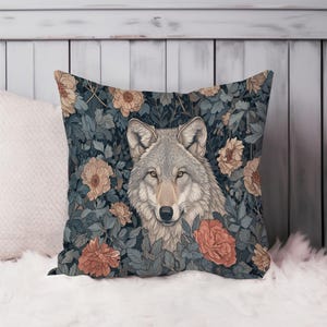 May include: Square decorative pillow featuring a detailed illustration of a wolf surrounded by flowers and foliage. The color palette includes shades of gray, peach, and dark blue, creating a nature-inspired design.