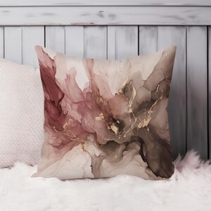 May include: A square throw pillow featuring an abstract alcohol ink design with flowing washes of dusty rose, deep brown, and cream colors. The pattern is accented with thin, vein-like metallic gold lines that create a marbled effect across the surface.