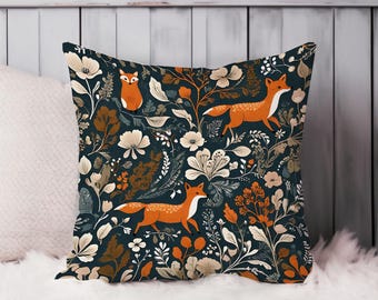 May include: Square throw pillow with a dark teal background featuring a repeating pattern of orange foxes, cream-colored flowers, and various foliage in shades of brown and green. The pillow is resting on a white, fluffy surface.