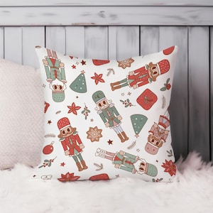May include: White square throw pillow with a repeating pattern of Christmas nutcrackers, trees, stars, and gifts in red, green, and brown. The pillow is decorated with a festive holiday design.