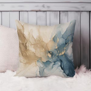May include: A square throw pillow featuring an abstract alcohol ink design with flowing swirls of beige, cream, and deep blue colors. The pattern includes thin, metallic gold veins that weave through the fluid shapes, creating a marbled effect.