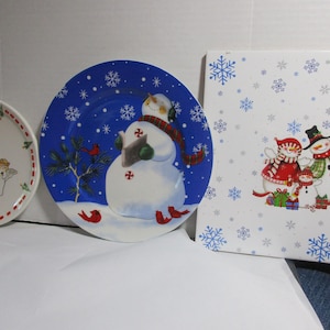 Puede incluir: Tres platos de cerámica con temática navideña de invierno. Un plato presenta un muñeco de nieve sosteniendo un bastón de caramelo, otro plato presenta una familia de muñecos de nieve y el tercer plato presenta un muñeco de nieve, un ángel y un Papá Noel.