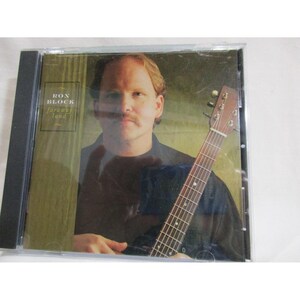 Könnte beinhalten: Eine CD-Hülle mit einem Mann mit Schnurrbart, der eine Gitarre hält. Das CD-Cover trägt den Text "RON BLOCK far away land" in Gold. Der Hintergrund ist ein gedämpftes Grün.