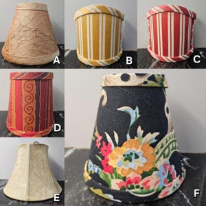 May include: A collection of six small lampshades in various designs. The shades include a textured tan shade, a yellow and white striped shade, a red and white striped shade, a shade with red and gold patterns, a beige suede shade, and a floral print shade.