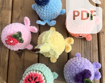May include: Six crocheted plush toys shaped like fruit. The toys are in various colors, including pink, blue, yellow, green, and purple. Each toy has a different fruit design, including a strawberry, a blueberry, a banana, a watermelon, and a grape.