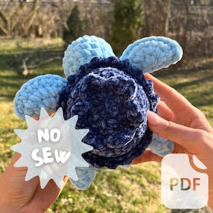 May include: A crocheted blue and navy turtle toy with the words "NO SEW" on a white starburst. The toy is being held by a person's hands. The image also includes the word "PDF" in a white box with a blue outline.