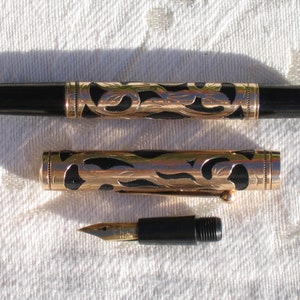 May include: A gold and black fountain pen with a decorative floral design. The pen is disassembled, showing the nib and the cap.