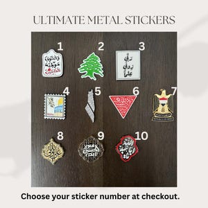 May include: Ten metal stickers with diverse designs and Arabic text are displayed. The stickers feature a green cedar tree, a stamp with a building, and a red triangle with Arabic script. The text "ULTIMATE METAL STICKERS" is at the top of the image.