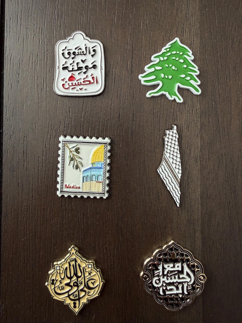 May include: A selection of decorative pins with diverse designs. Includes a green tree, a stamp with a mosque, a map outline, and pins with Arabic calligraphy. The pins are in various shapes and colours, with intricate details.