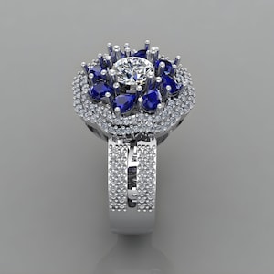 May include: A silver ring with a large round center stone surrounded by smaller blue pear-shaped stones and a halo of smaller round stones.