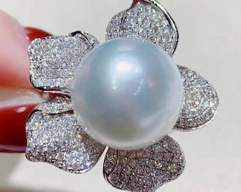 May include: A white pearl ring with a flower design. The flower is made of white metal and is set with small diamonds. The pearl is large and round.