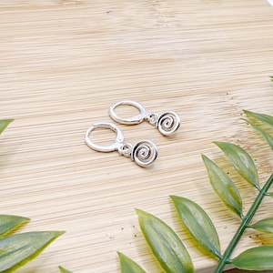 Puede incluir: Un par de pendientes de aro de plata con un encanto en espiral que cuelga de cada aro.