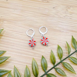 May include: A pair of silver hoop earrings with red, white, and green candy cane-inspired charms.