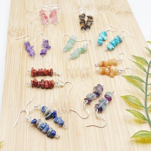Puede incluir: Surtido de pendientes de piedras preciosas con ganchos de plata. Los pendientes presentan diferentes colores y formas de piedras, incluyendo rojo, verde, azul, morado y marrón.