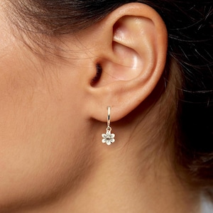 May include: Silver hoop earrings with a small flower charm dangling from each hoop.