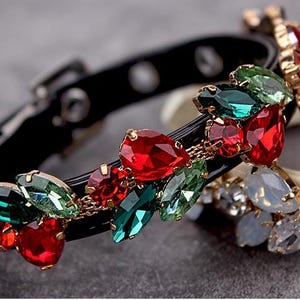 May include: A black leather dog collar with a decorative trim of red, green, and gold rhinestones. The rhinestones are arranged in a floral pattern.
