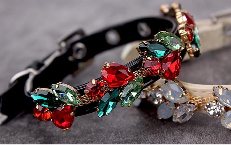 May include: A black leather dog collar with a decorative trim of red, green, and gold rhinestones. The rhinestones are arranged in a floral pattern.