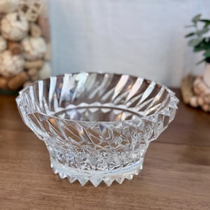 May include: A clear glass bowl with a geometric design. The bowl has a wide, shallow base and a tall, narrow rim. The bowl is made of thick, heavy glass and has a polished finish.