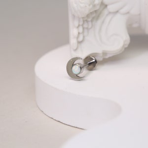 May include: A silver crescent moon body jewelry with a white opal gemstone.