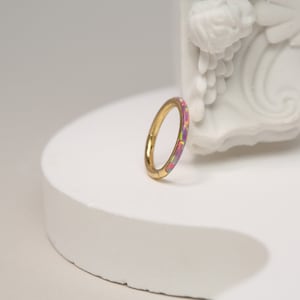 Op de afbeelding: Een gouden ring met een dunne band en een kleurrijke opaal inlay. De opaal is een mix van roze, paars en groen.