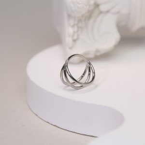 Puede incluir: Un pendiente de aro triple plateado para un piercing de cartílago. El aro está hecho de tres anillos entrelazados.
